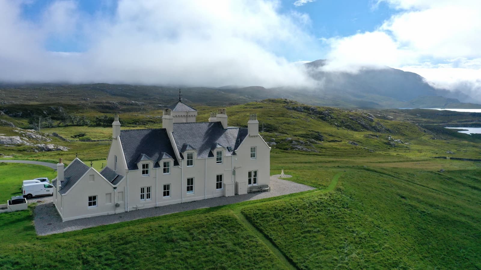 Large white house in a scenic landscape with mountains and green fields.