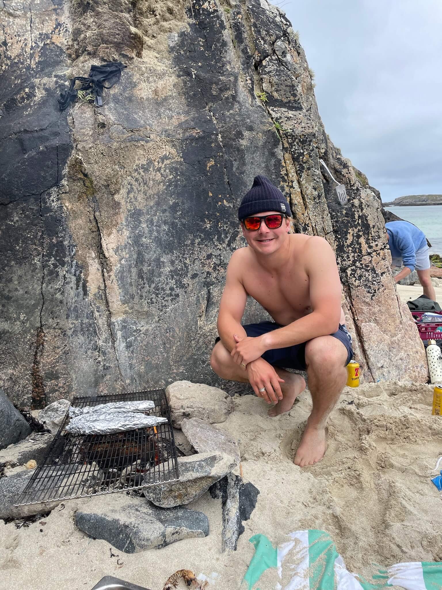 Boy barbecuing fresh mackerel on the beach near Uig Lodge, enjoying a traditional outdoor cooking experience by the sea.
