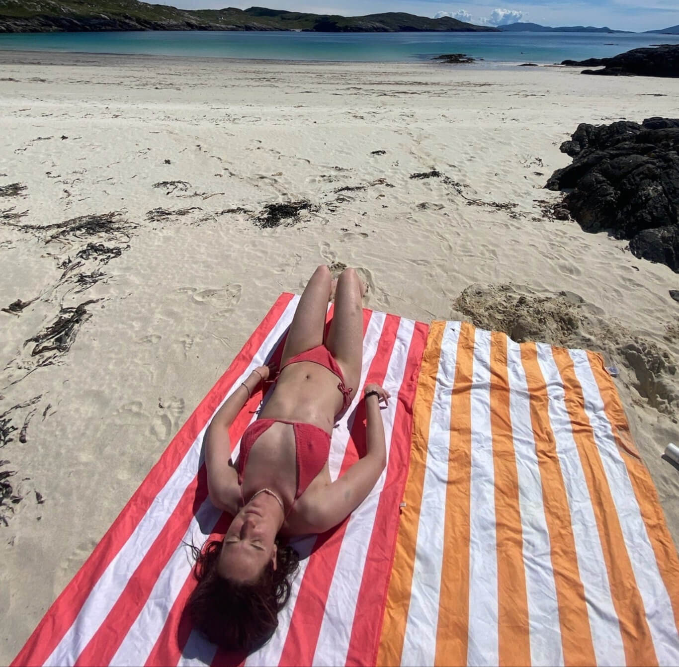 Girl sunbathing on a white sandy beach with turquoise waters near Uig Lodge, capturing the relaxing coastal atmosphere of the Isle of Lewis.