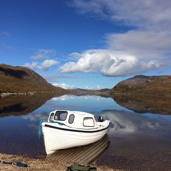 View of Loch Suainaval with a small boat on the Isle of Lewis, surrounded by rolling hills and natural Hebridean landscape