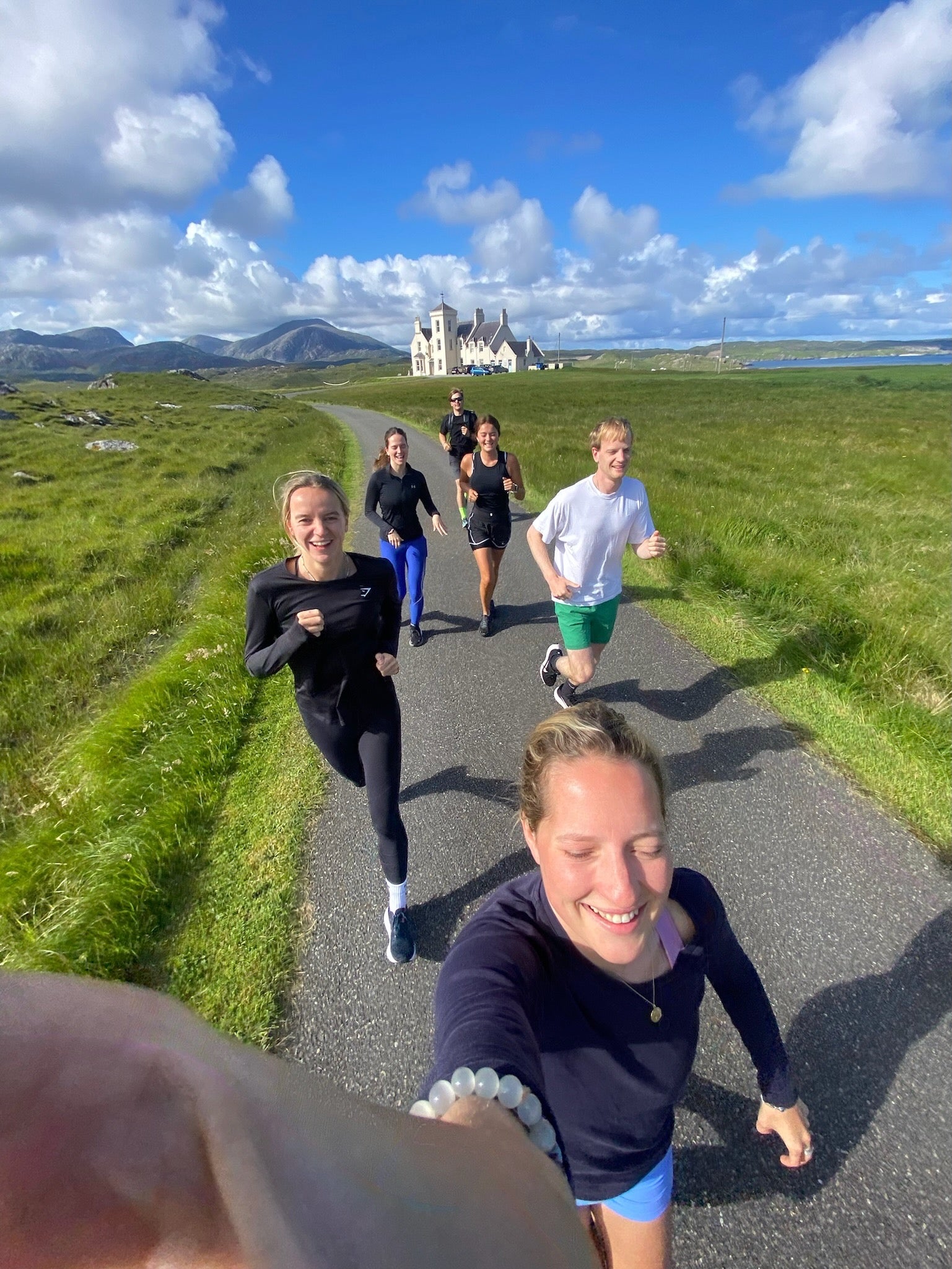 Group of fit runners setting off from Uig Lodge, with lush green landscape and clear blue skies in the background