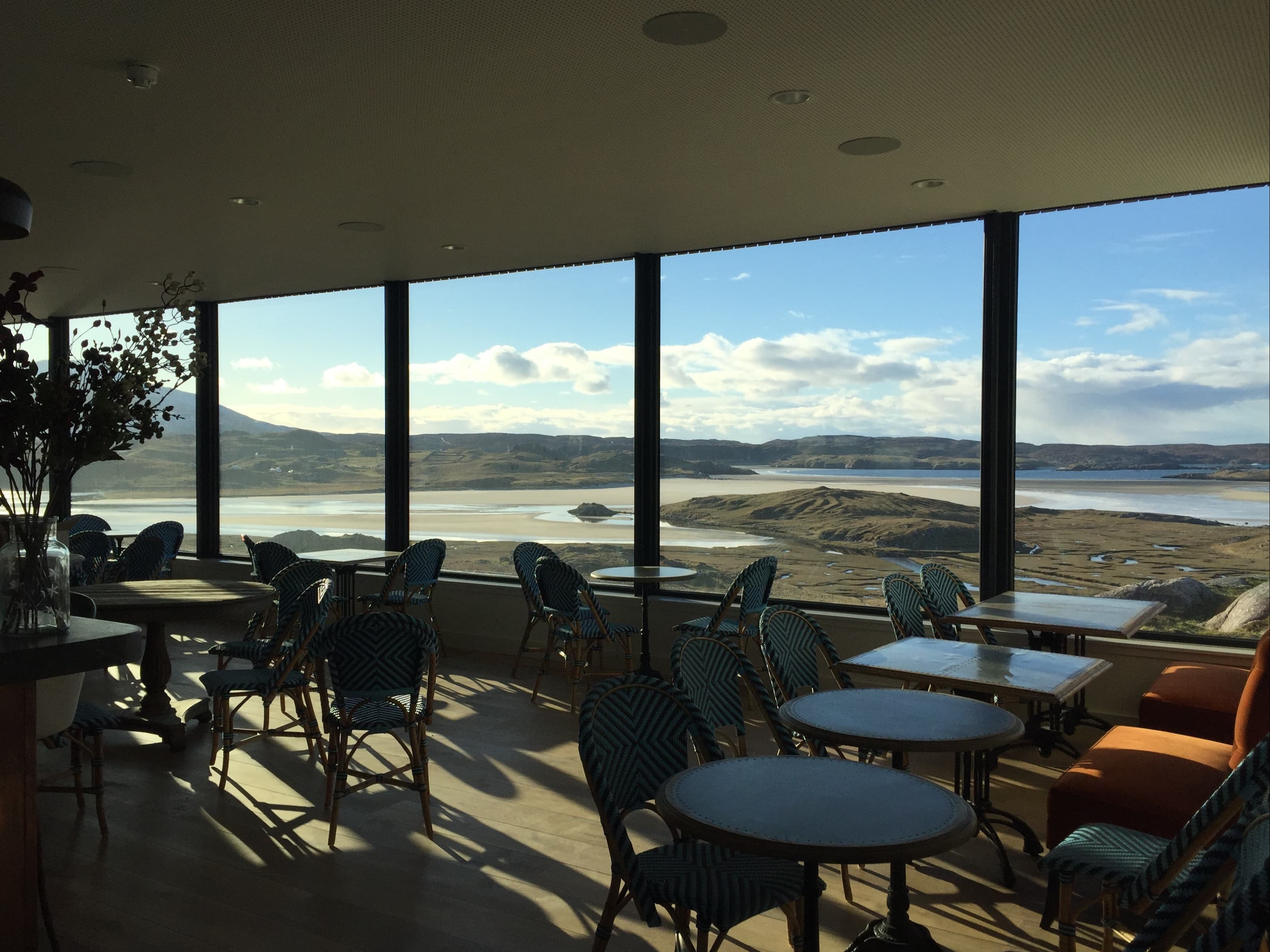Restaurant interior with large windows offering a scenic view of uig bay.