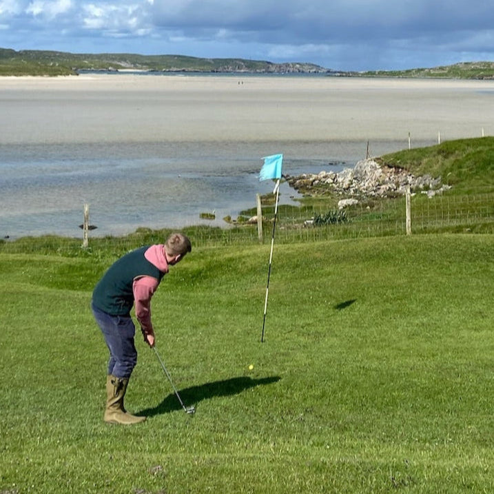 Young man hitting golf balls on Uig Lodge private golf course, overlooking Uig bay